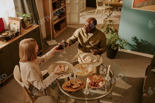 Preview: Senior Caucasian Woman and Senior Black Man Clinking Glasses Sharing Romantic Dinner