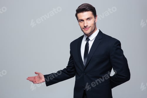 Preview: Businessman With Arm Out In A Welcoming Gesture Over Gray Background