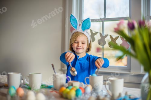 Preview: Boy at table wearing bunny ears decorating eggs for Easter