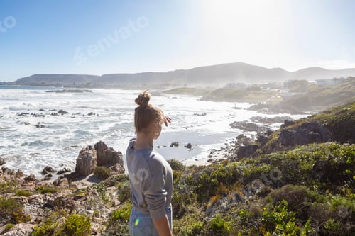 Preview: A teenage girl on rocks, looking at the coastline, waves breaking and mist rising.