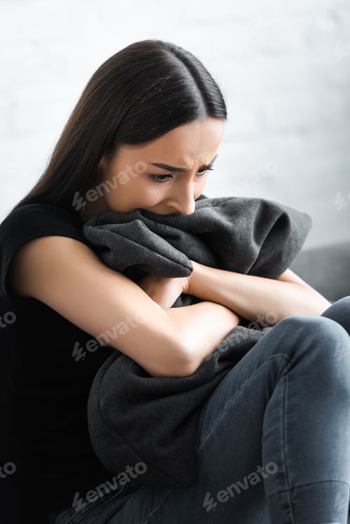 Preview: despaired young woman hugging pillow while suffering from depression at home