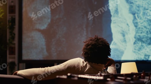 Preview: Man watching travel documentary with beautiful cinematography on modern video projector