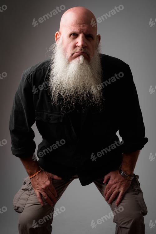 Preview: Stressed mature bald man with long beard looking angry while leaning forward