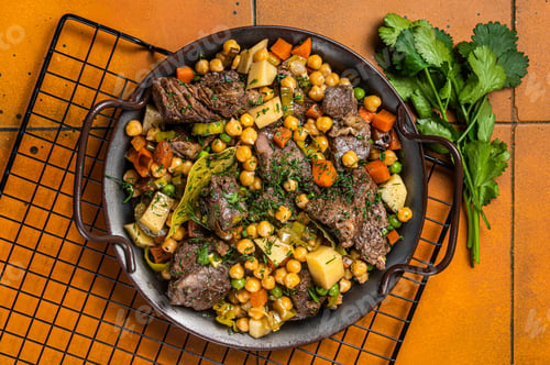 Preview: Spanish cocido Madrid stew with chickpeas, meat, carrots and potatoes. Orange background. Top view