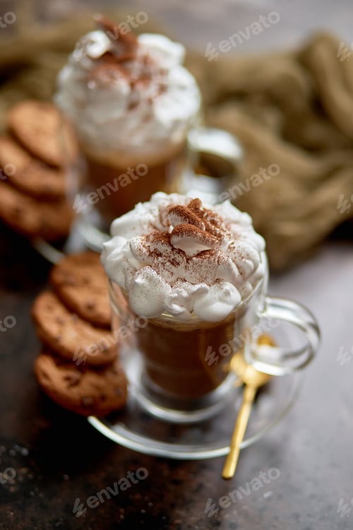 Preview: Two tall glasses with hot chocolate, whipped cream and cinnamon powder on top