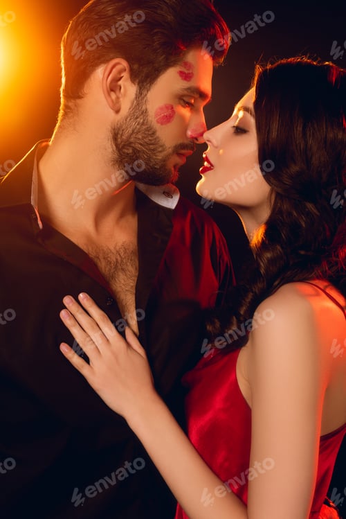 Preview: Beautiful woman kissing handsome boyfriend with lipstick prints on face on black background with
