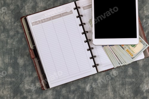Preview: Workplace with paper diary notebook with one hundred dollar bills on digital smart tablet