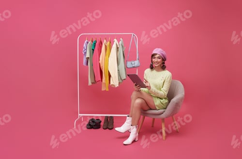 Preview: Young smiling beautiful asian woman making online shopping and sitting on chair with new clothes
