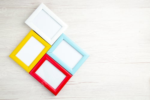 Preview: Above view of four empty picture frames in different colors on wooden stripped background