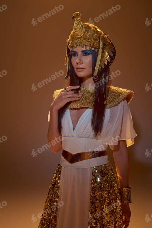 Preview: Brunette woman in egyptian headdress and stylish look posing on brown background with lighting