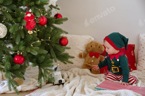 Preview: Baby girl dressed as elf sitting in front of Christmas tree