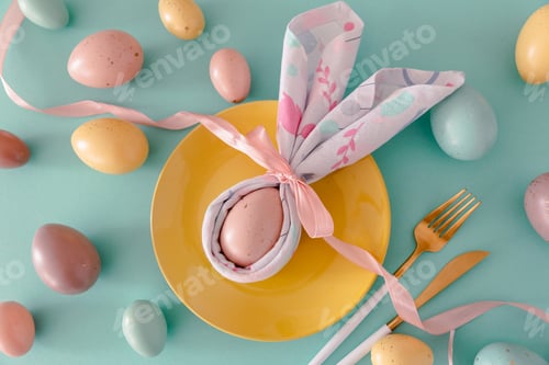 Preview: Plate decorated bunny ear napkin, white tulips and Easter eggs on blue background.