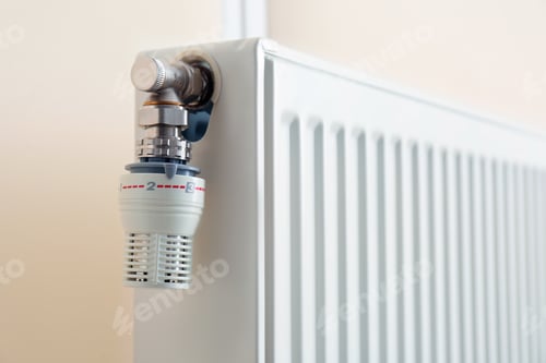 Preview: Heating radiator with thermostat near light wall, closeup