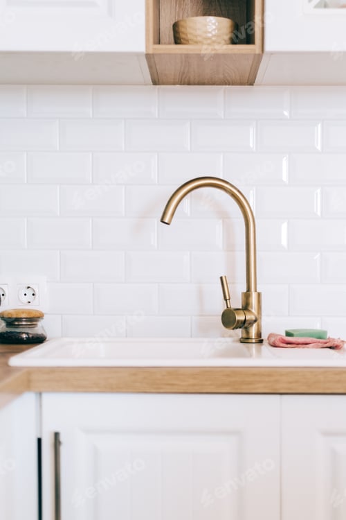 Preview: Golden faucet or water tap with metal washing sink in the kitchen.