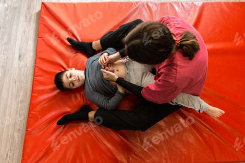 Preview: disabled child and physiotherapist on a red gymnastic mat doing exercises. pandemic mask protection