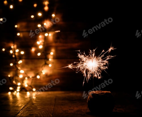 Preview: burning sparkler and christmas lights on wooden background