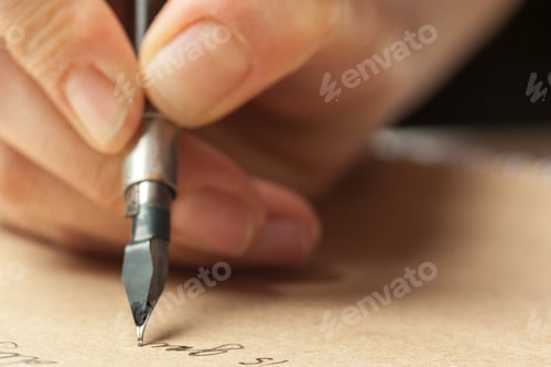 Preview: Detail of hand holding a pen writing on brown paper in a warm indoor setting