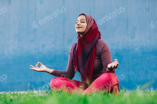 Preview: Woman meditates in grassy area near blue wall
