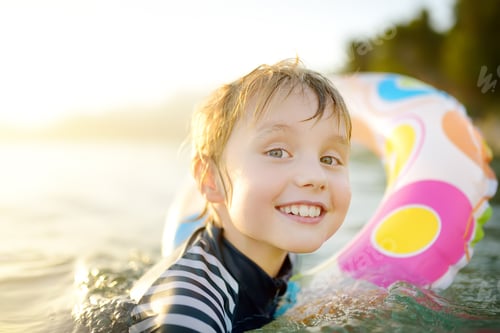 Preview: Little boy swimming with colorful floating ring in sea on sunny summer day.