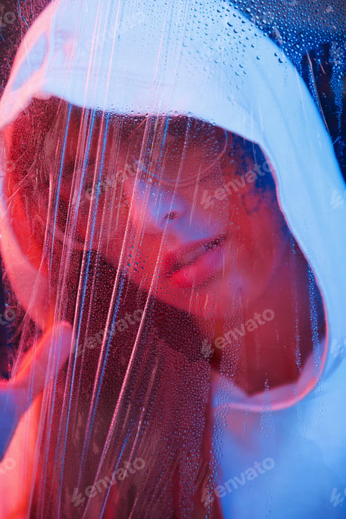 Preview: Through the glass. Studio shot in dark studio with neon light. Portrait of young girl
