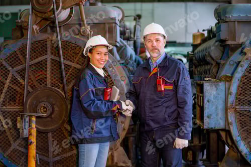 Preview: Factory worker or technician stand and shake hands with Asian factory woman in front of big machine