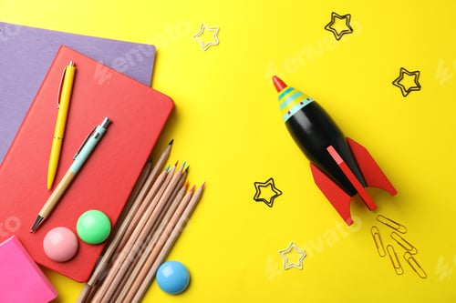 Preview: Bright toy rocket and school supplies on yellow background, flat lay