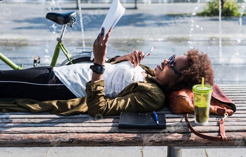 Preview: Smiling woman lying on a bench reading notes