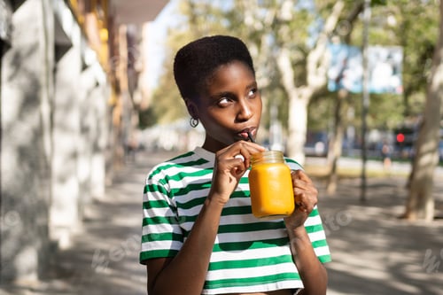 Preview: Happy African woman, drinking orange fruit juice with a straw