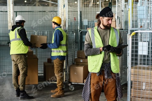 Preview: Young engineer in reflective jacket looking at tablet screen while networking