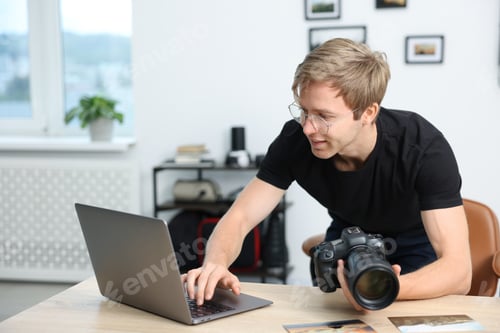 Preview: Professional photographer with camera working on laptop at table in studio