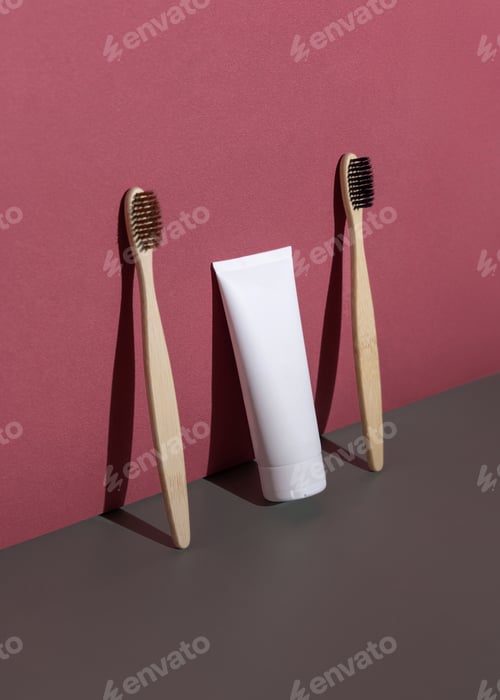 Preview: Blank toothpaste tube and bamboo toothbrushes on grey and red, hard shadow closeup, mockup