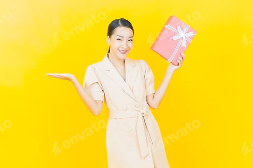 Preview: Smiling Woman Holding Gift Box Against Yellow Background