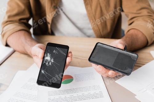 Preview: Cropped view of businessman showing disassembled smashed smartphone at workplace on blurred