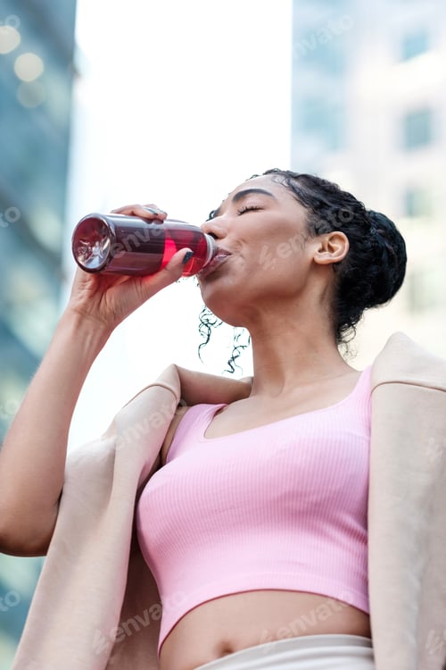Preview: Relaxed young fitness woman drinking energy drink outdoors.