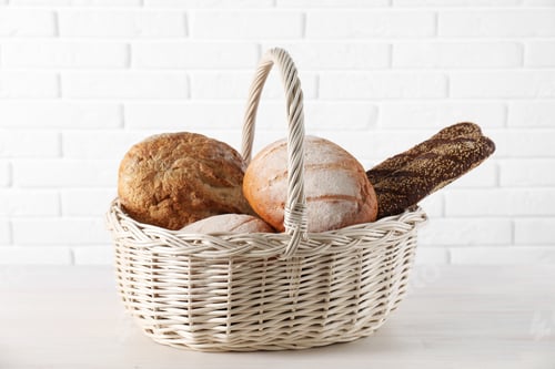 Preview: Different types of bread in wicker basket on white wooden table