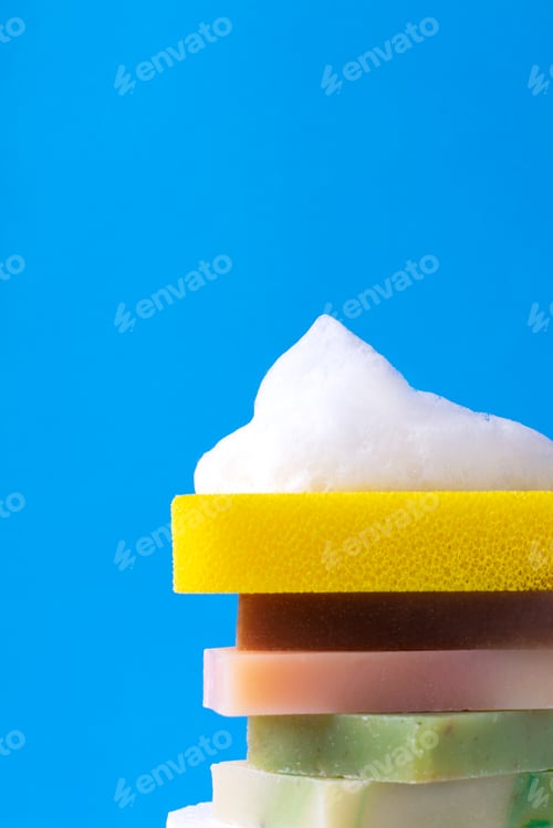 Preview: Stack with body sponge with foam on different bars of soap against the blue background.