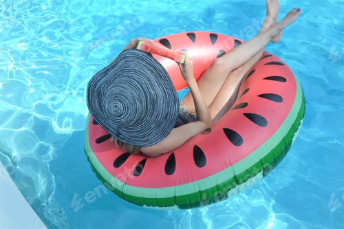 Preview: Beautiful woman wearing summer hat floating at the swimming pool in a watermelon float