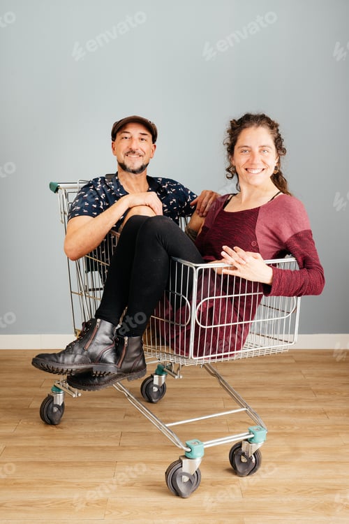 Preview: Smiling Man and Woman Sitting in a Shopping Cart at Home