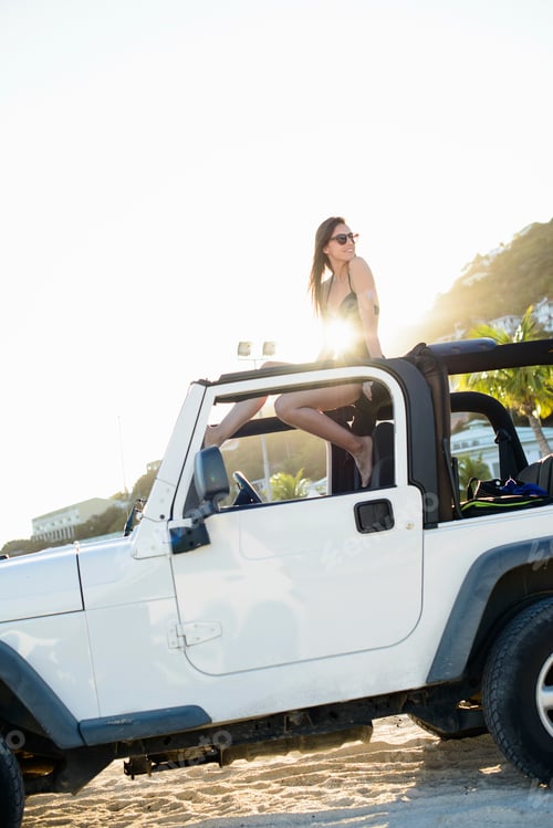 Preview: Woman sitting on roof of jeep on beach