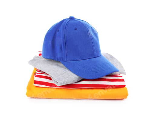 Preview: Blue baseball cap and stack of folded t-shirts isolated on white. Mockup for design