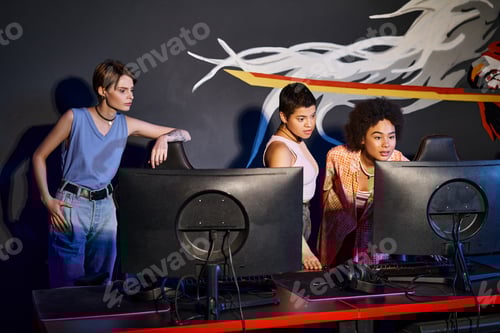 Preview: Team of young gamers at a cybersport event, interracial women looking at computer while playing game