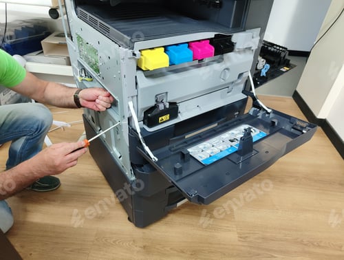 Preview: Man fixing the printing machine with open lid and visibly colorful ink containers