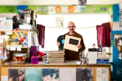 Preview: Portrait of mature man in record shop, putting record into record sleeve