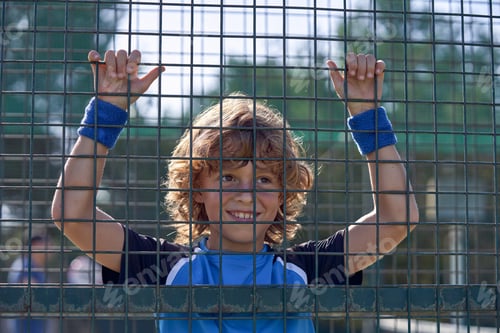 Preview: Cheerful boy hanging on metal fence on court on sunny day