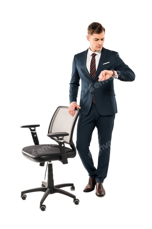 Preview: confident businessman standing near chair and looking at watch isolated on white