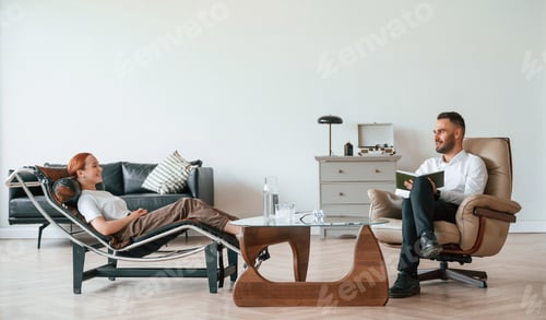Preview: Side view. Woman is sitting in chair at an appointment with a psychologist