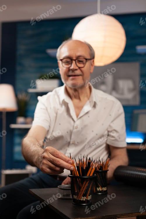 Preview: Senior caucasian man sitting at art studio desk with pencils