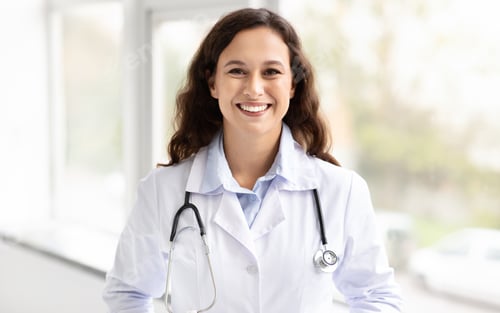 Preview: Cheerful millennial woman general physician standing by window