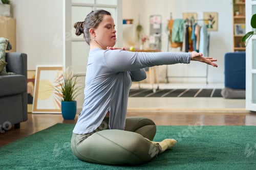 Preview: Side view of girl with Down syndrome sitting on the floor with crossed legs