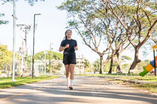 Preview: Asian woman in black sportswear exercising by running or jogging on the road in park under sunlight.